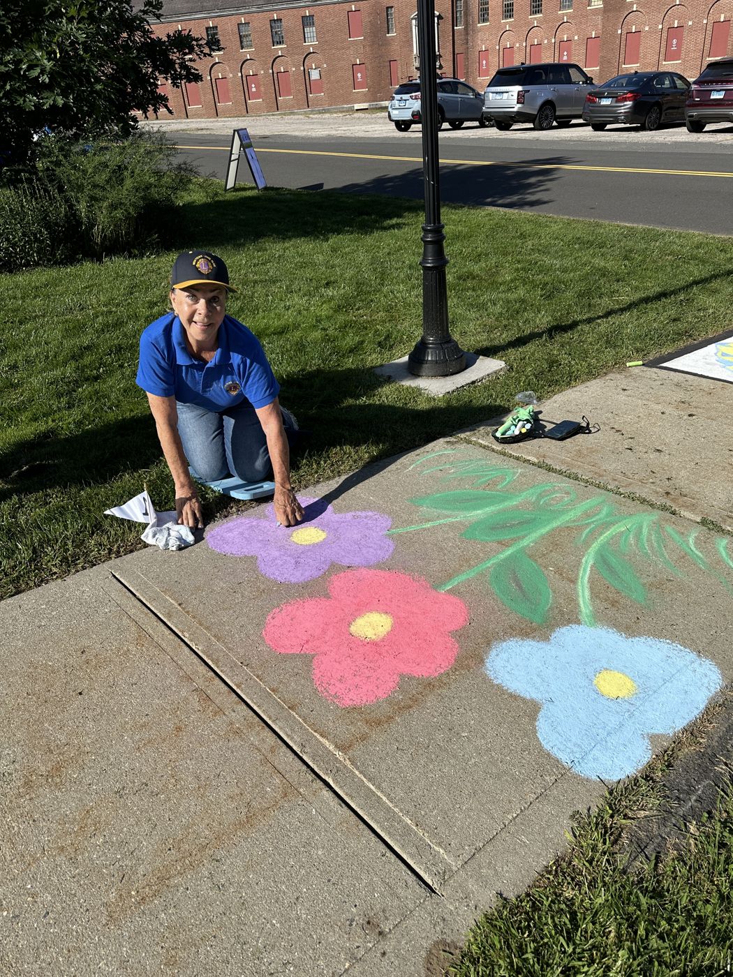 A Newtown Lion chalking bright flowers on the sidewalk